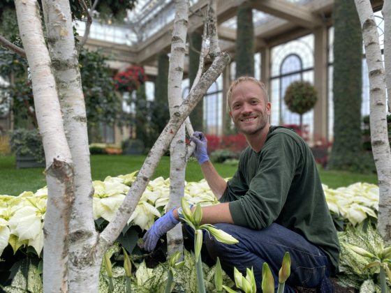 a person kneeling down in a garden bed looking and smiling at the camera